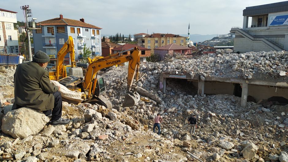 An elderly man watches bulldozers clearing building rubble.